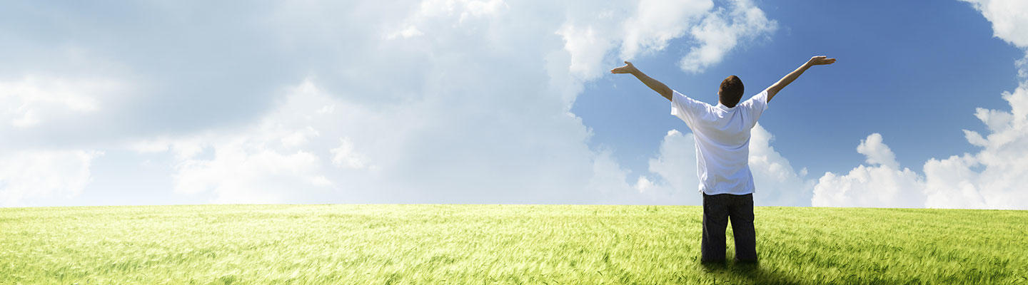 Homme debout dans l'herbe bras levés vers le ciel